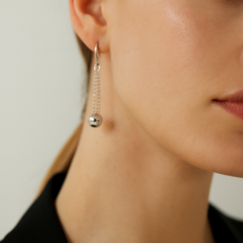 Silver earring with a chain and ball detail.