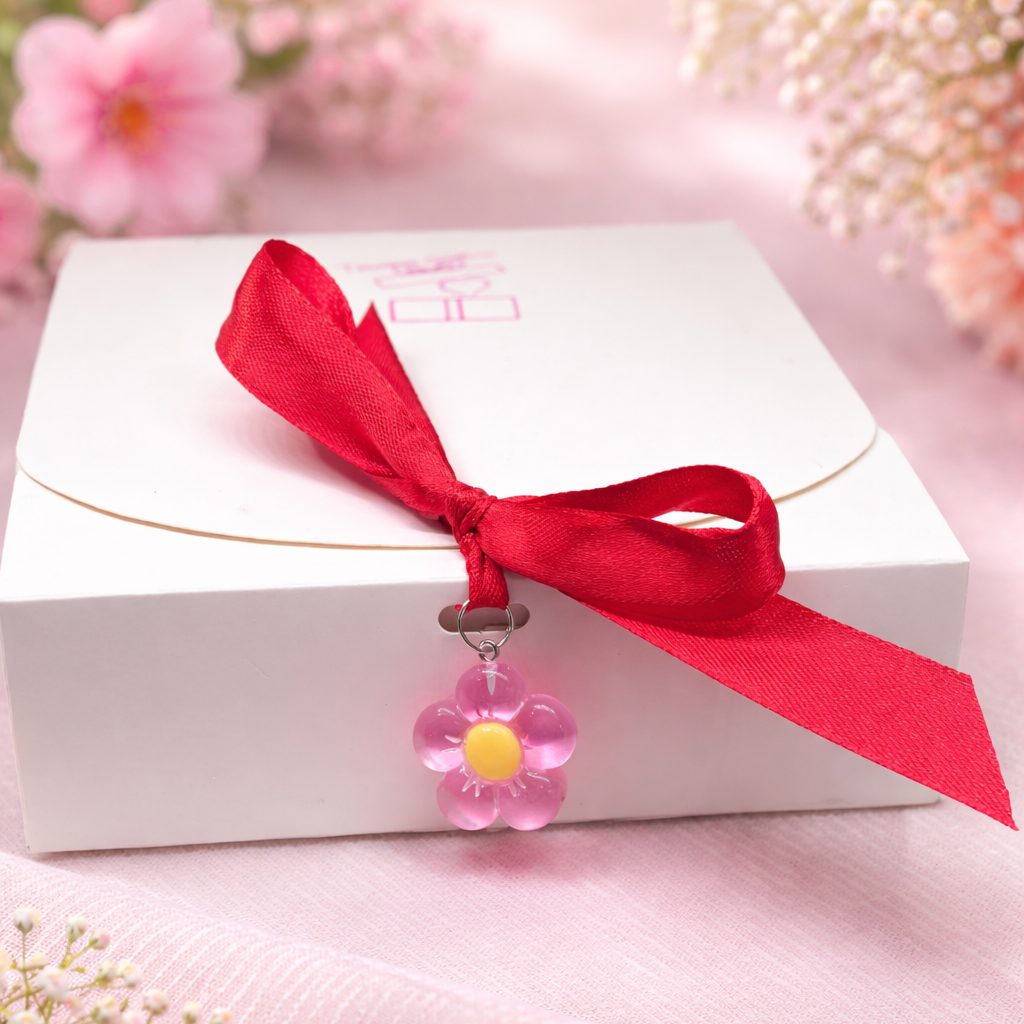 White gift box with a red ribbon and pink flower charm.