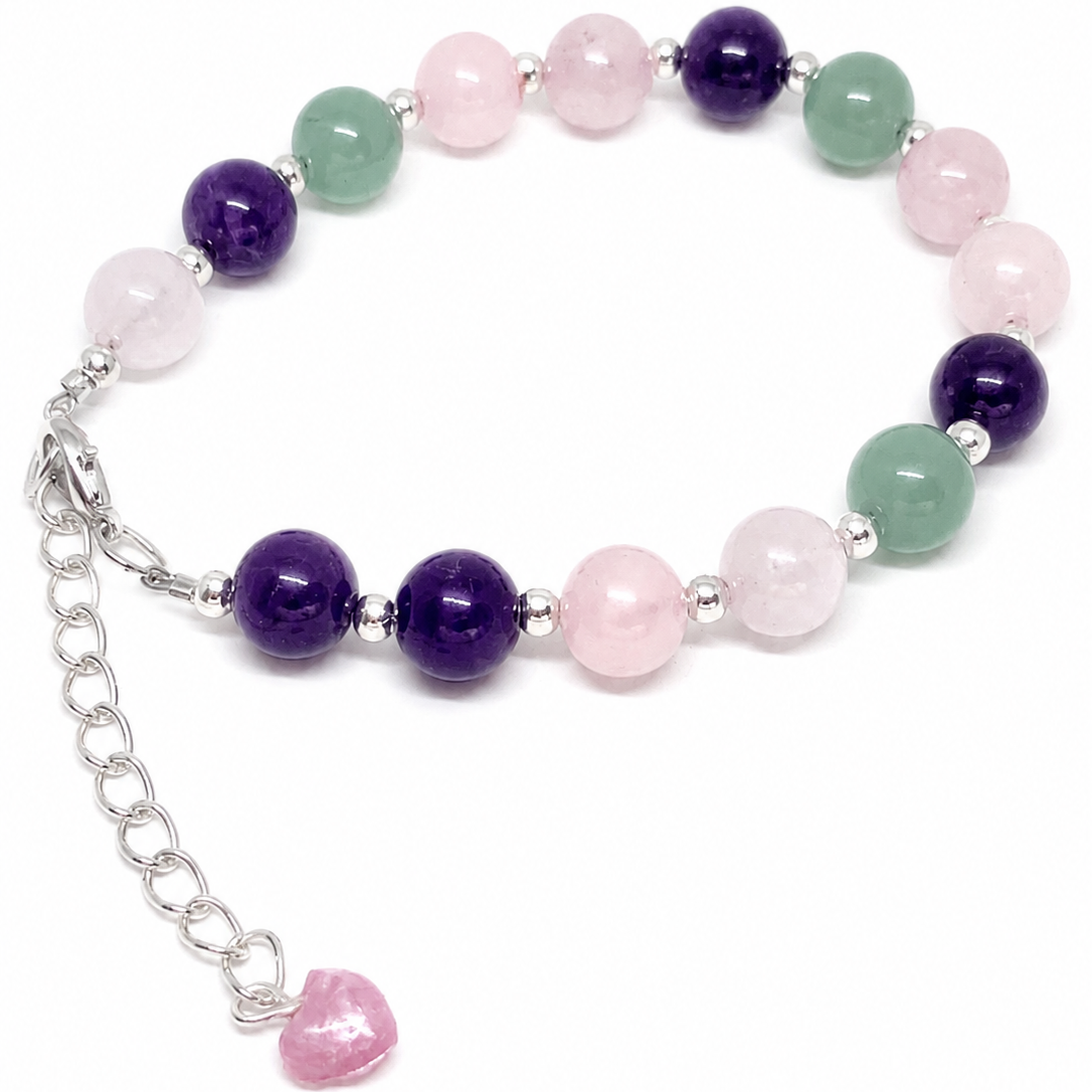 A beaded bracelet featuring polished purple amethyst, pink rose quartz, and green aventurine beads separated by small silver spacer beads, with a silver lobster clasp and an adjustable chain ending in a dangling pink heart charm.